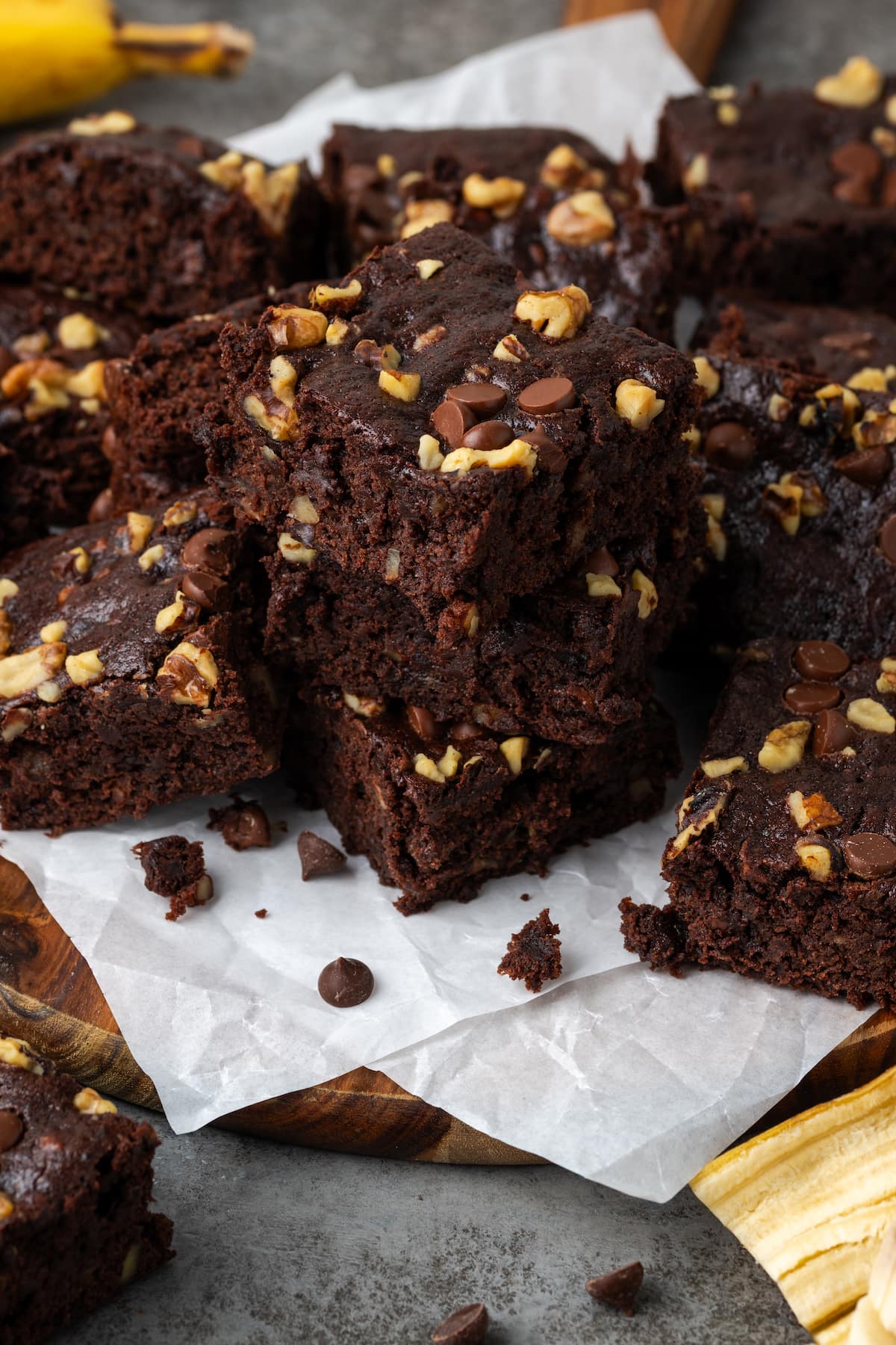 Assorted banana bread brownies stacked on top of a wooden platter lined with parchment paper.