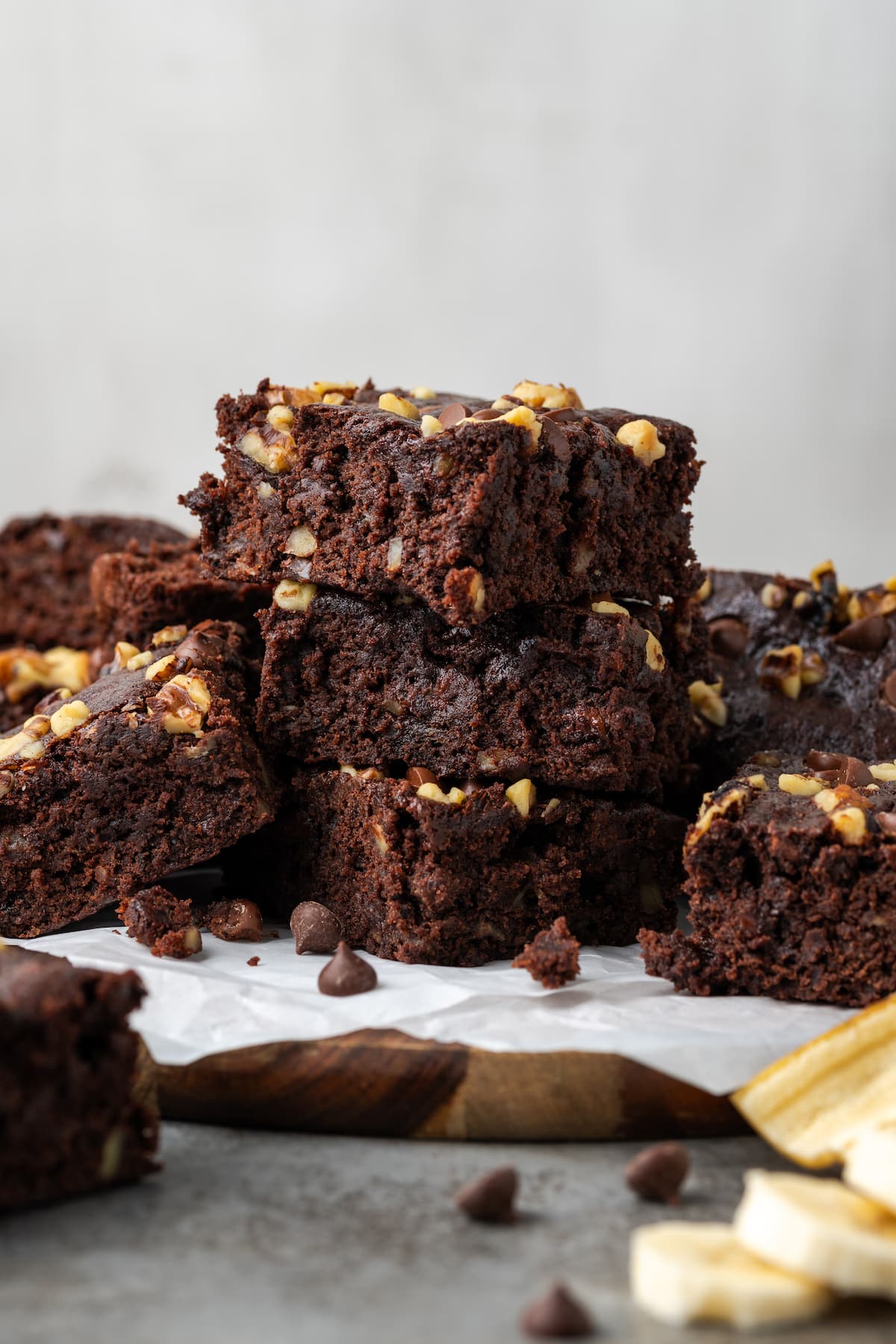 Side view of banana bread brownies stacked on top of a wooden platter lined with parchment paper.