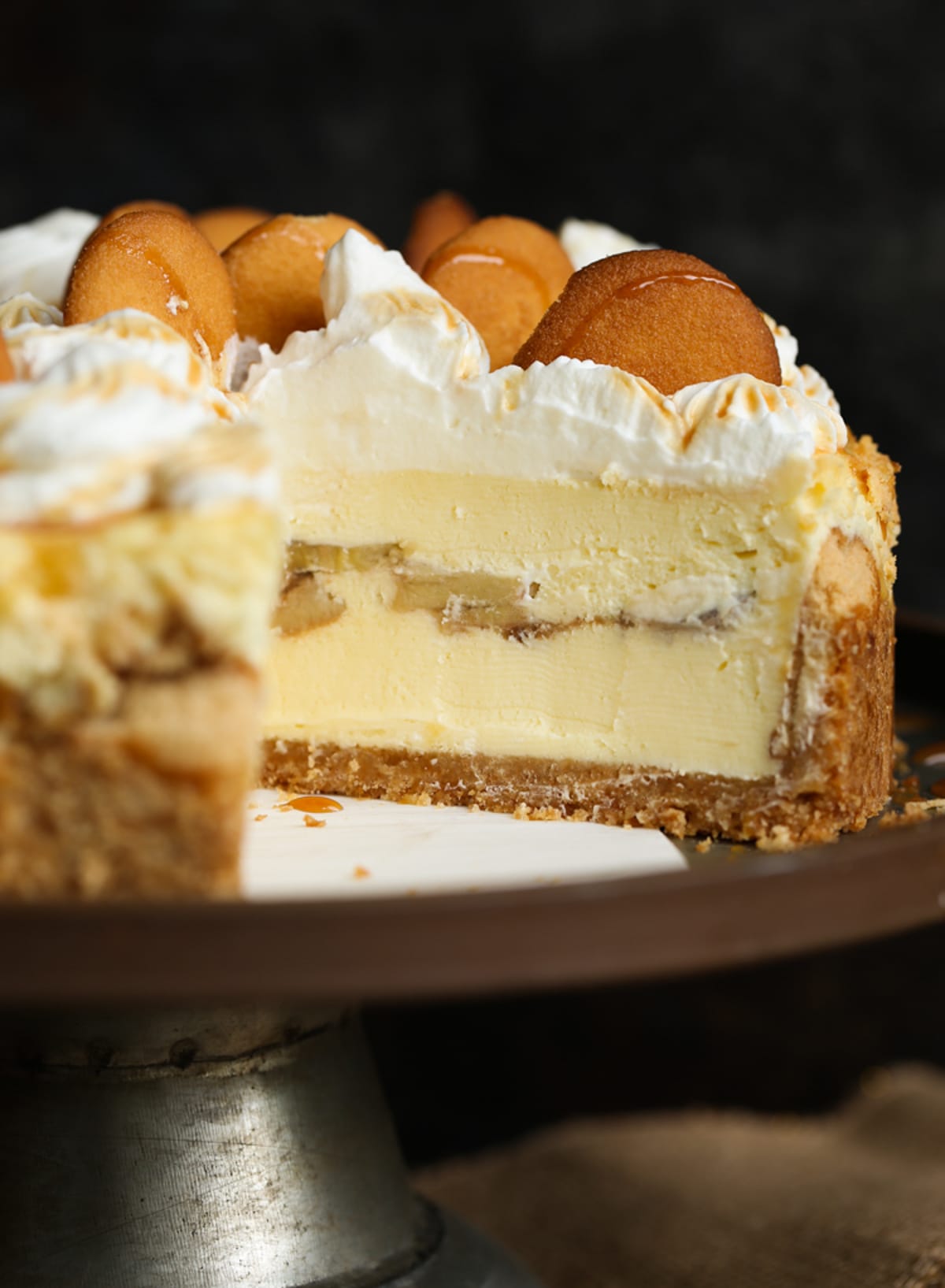 Banana pudding cheesecake on a cake stand with a slice missing.