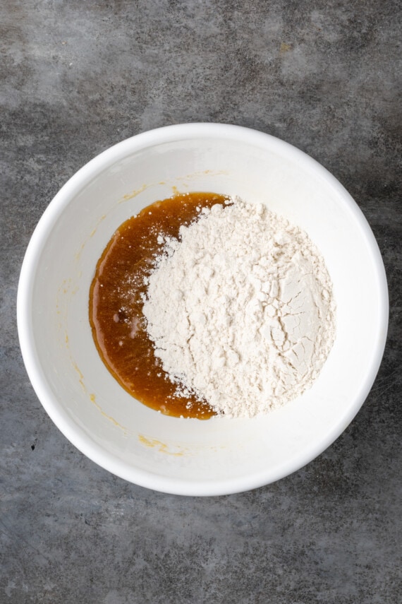 Flour added to wet cookie dough ingredients in a white bowl.