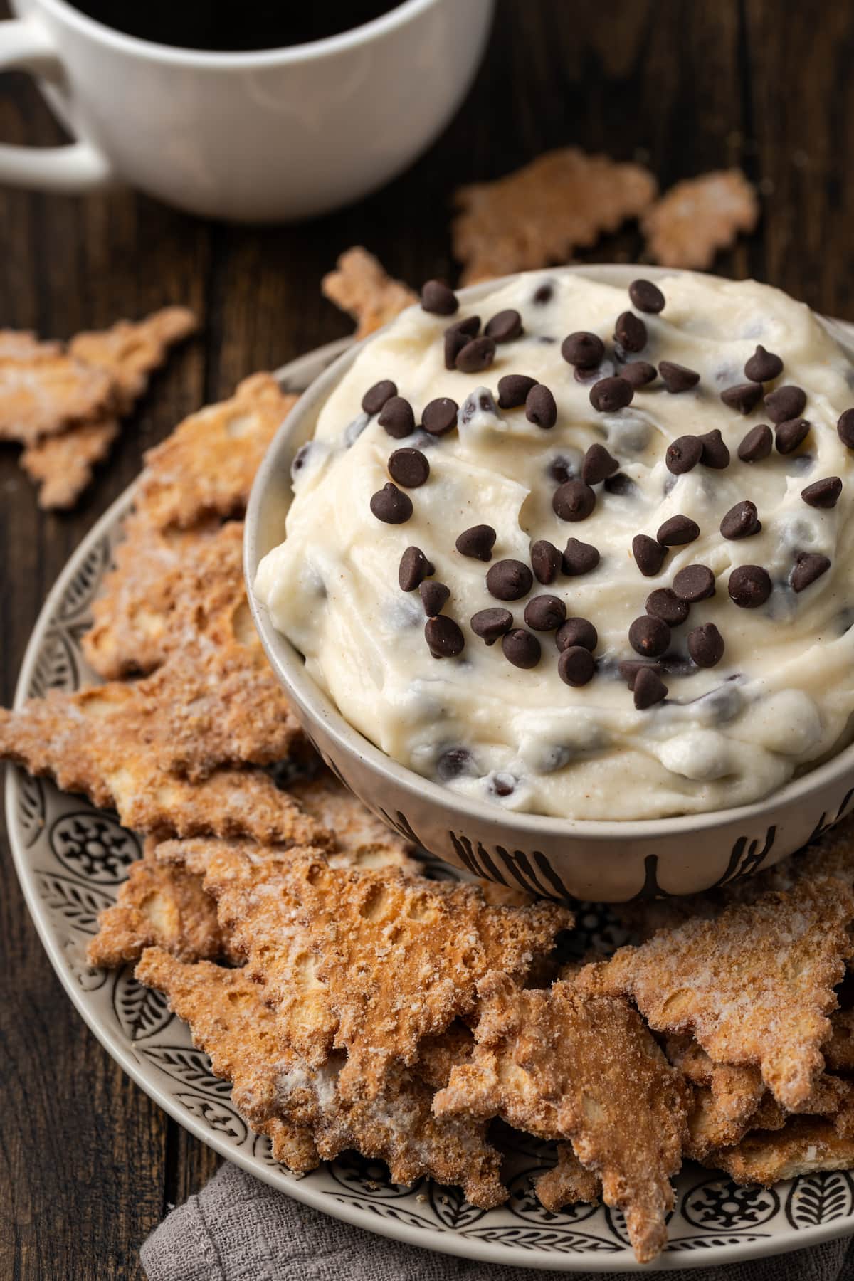 Cannoli dip served in a bowl, surrounded by cookies on a plate.