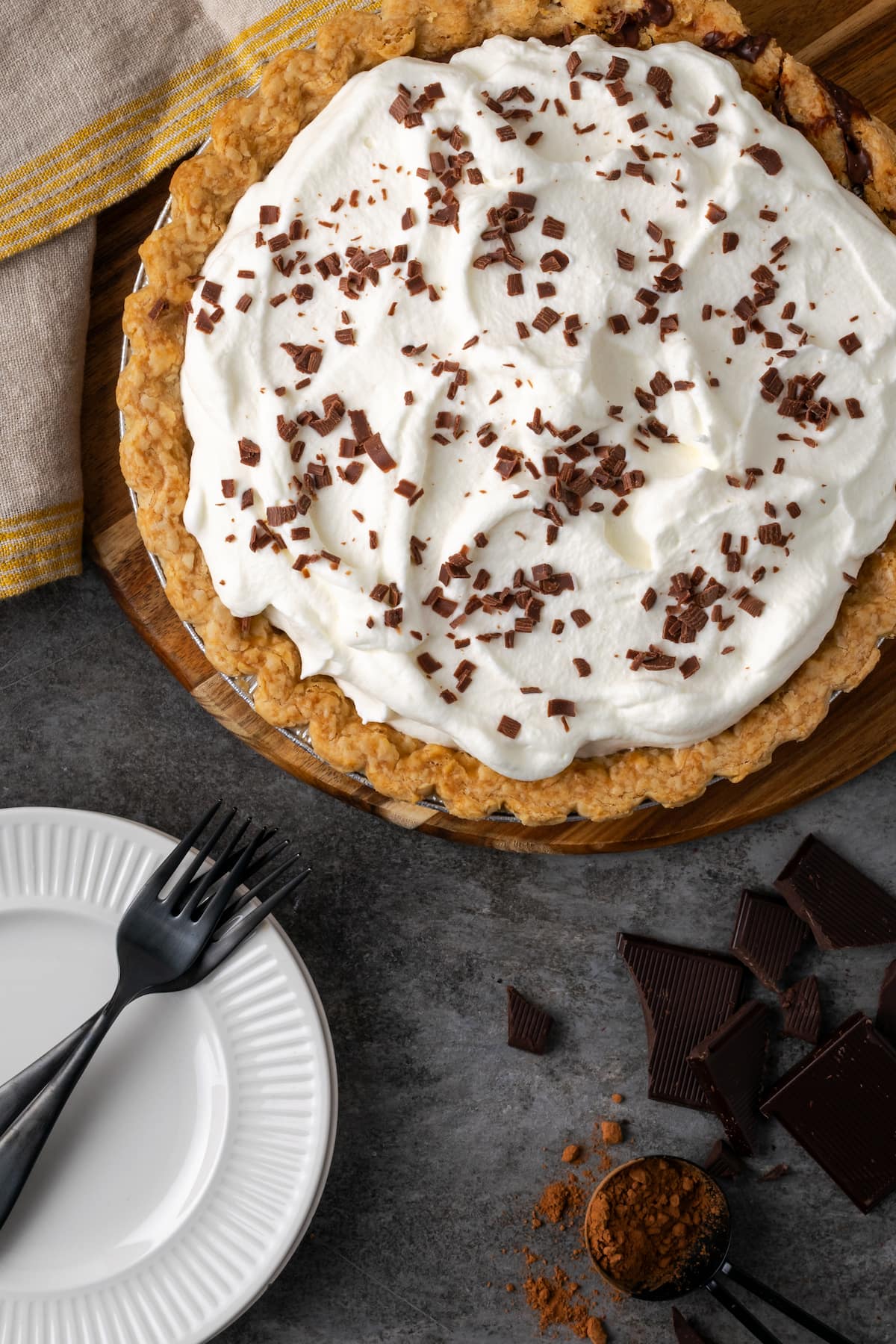 Overhead view of chocolate pudding pie topped with whipped cream and chocolate shavings, next to a fork on a white plate.