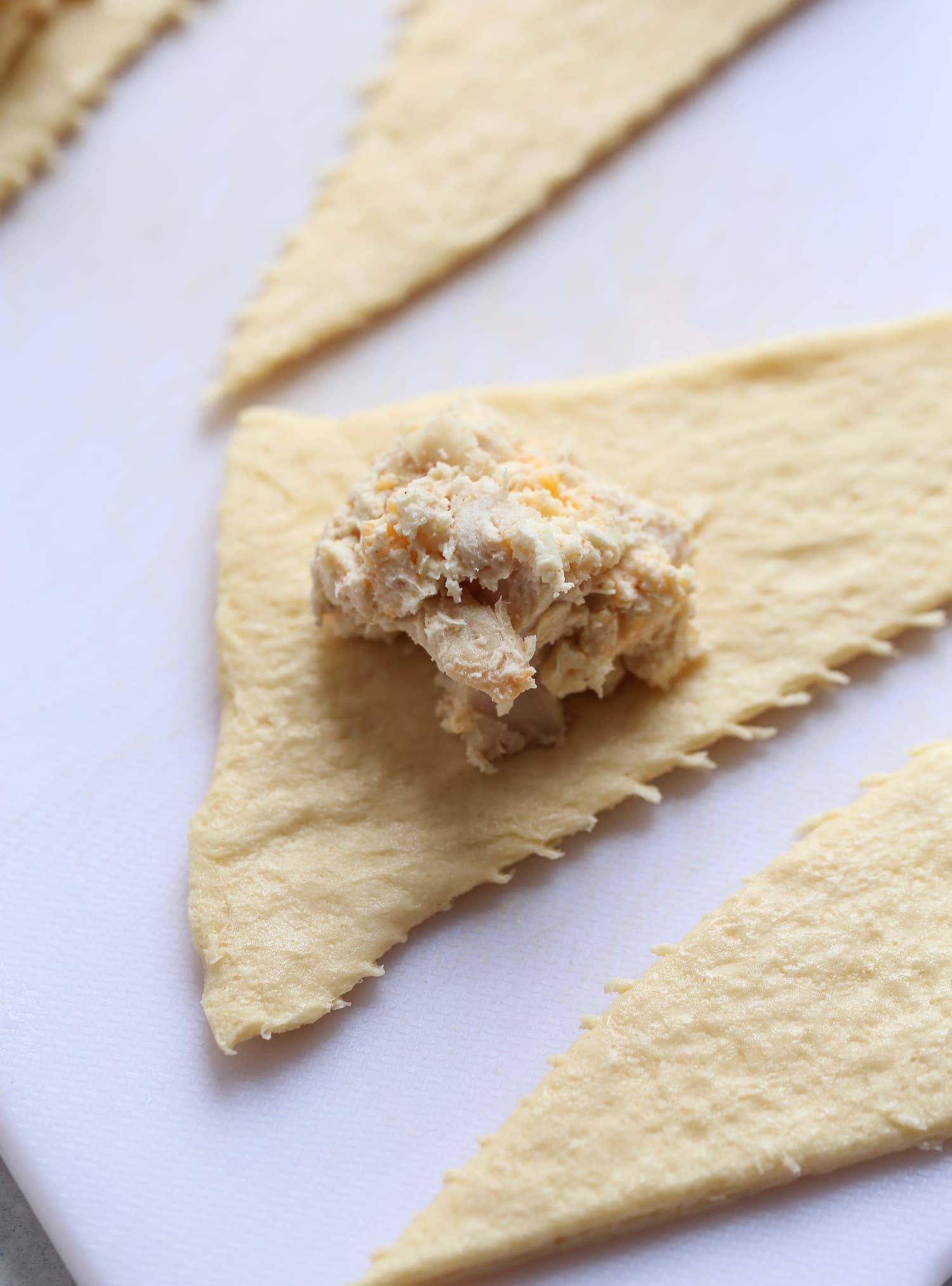 A tablespoon of chicken and cheese mixture on a triangle of crescent roll dough.