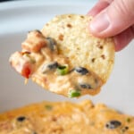 A hand holding a chip dipped in Crock Pot chicken nacho dip.