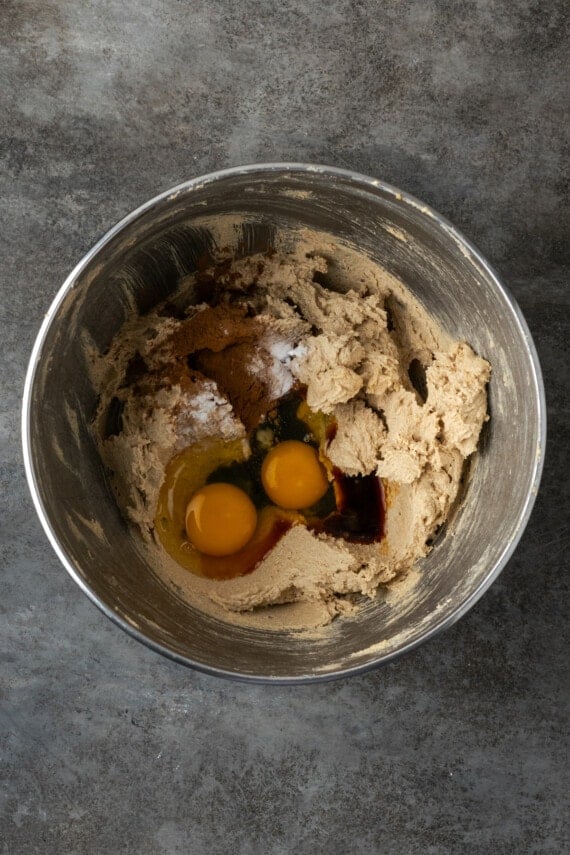 Eggs and vanilla added to creamed butter and sugar in a metal mixing bowl.