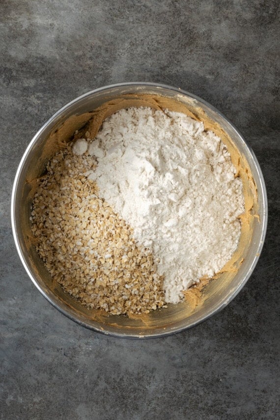 Dry ingredients and oats added into the wet cookie dough ingredients in a metal bowl.