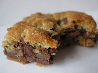 A chocolate chip cookie bar on a white surface with a bite missing.