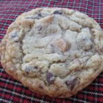 Overhead view of a toffee chip chocolate chip cookie on a plaid background