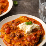 A bowl of lasagna soup topped with ricotta cheese and basil leaves.