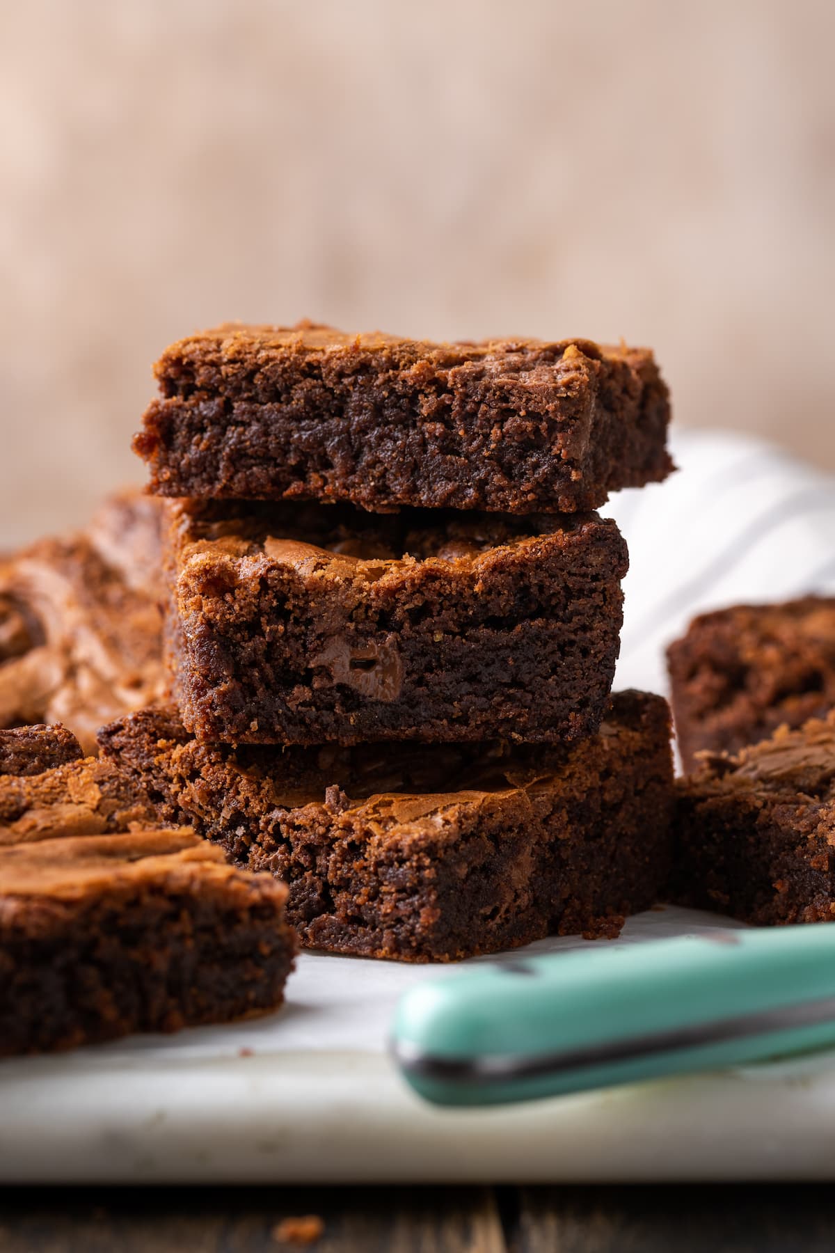 Three Nutella brownies stacked on top of one another on a cutting board, surrounded by more brownies.