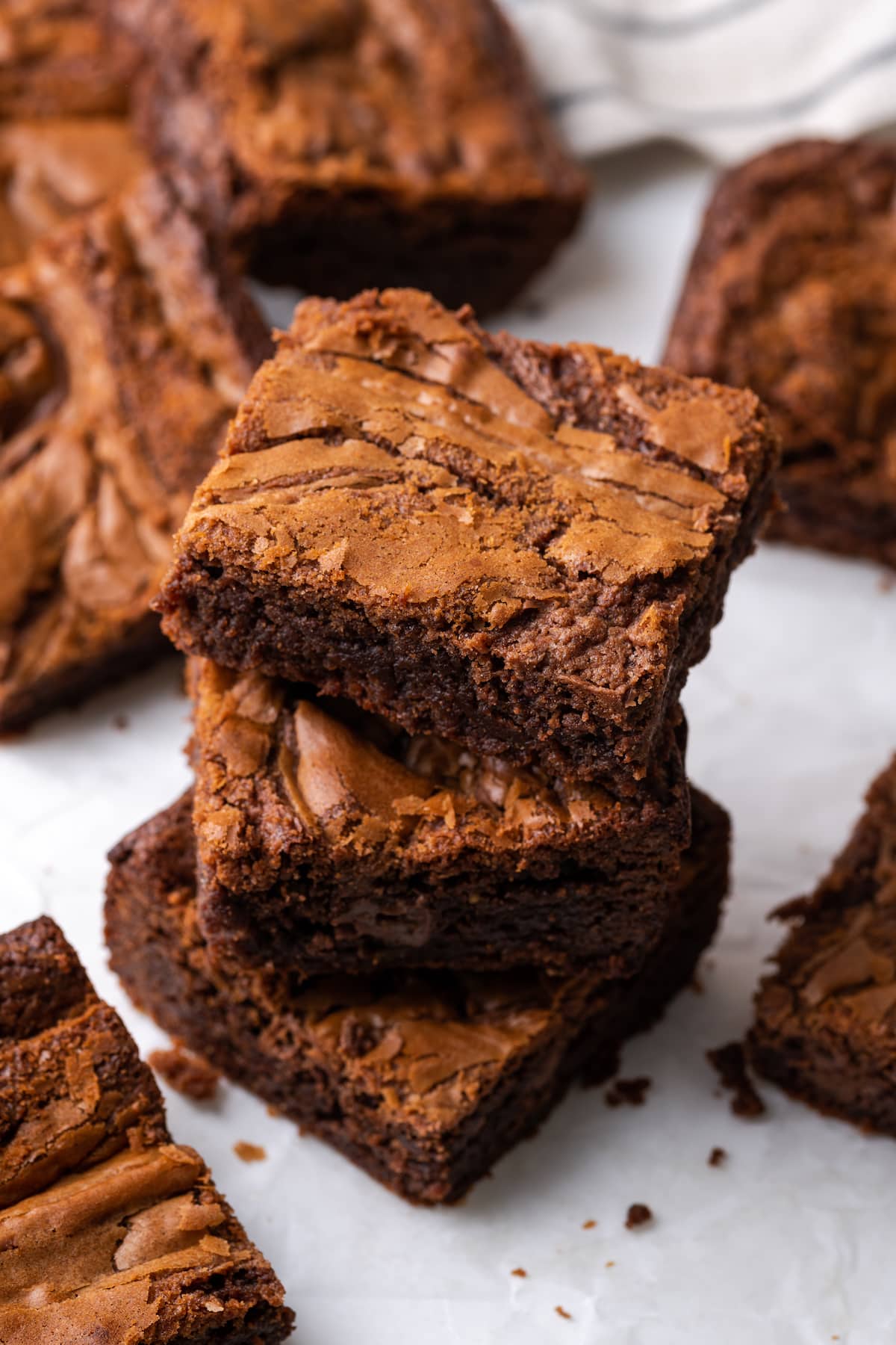 Overhead view of three Nutella brownies stacked on top of one another on a cutting board, surrounded by more brownies.