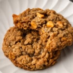 Two oatmeal butterscotch cookies stacked on a white plate, with a bite missing from the top cookie.