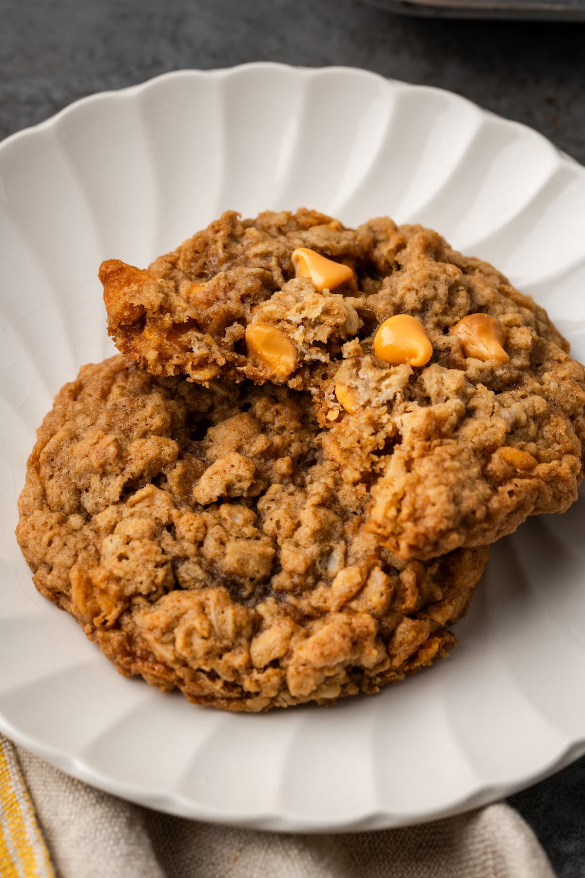 Two oatmeal butterscotch cookies stacked on a white plate, with a bite missing from the top cookie.