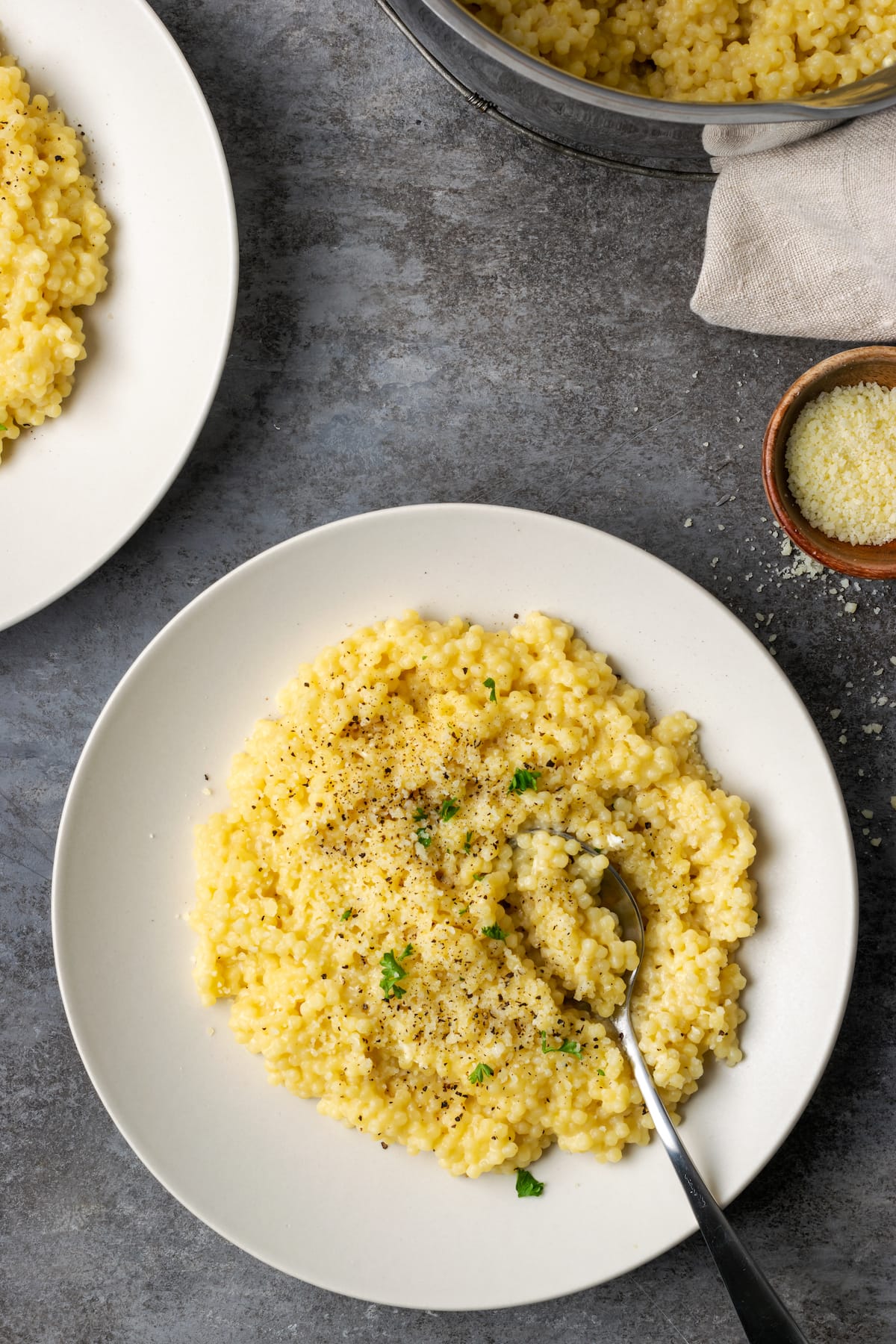 Overhead view of pastina served on a white plate topped with black pepper and parmesan.