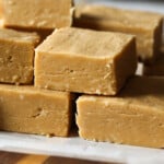 Peanut butter fudge squares stacked on top of each other on a piece of parchment paper.