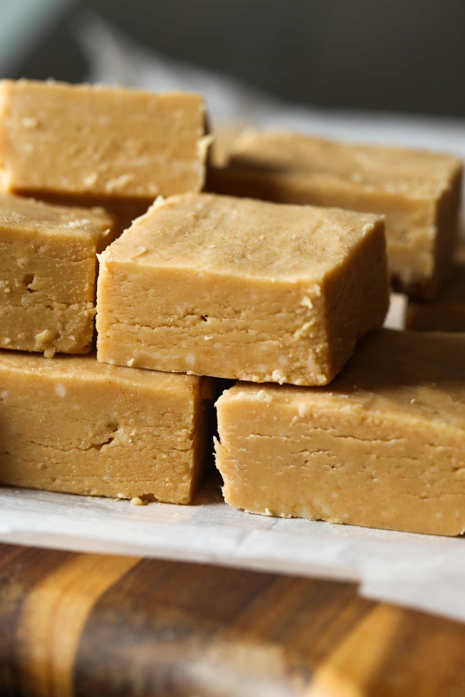 Peanut butter fudge squares stacked on top of each other on a piece of parchment paper.