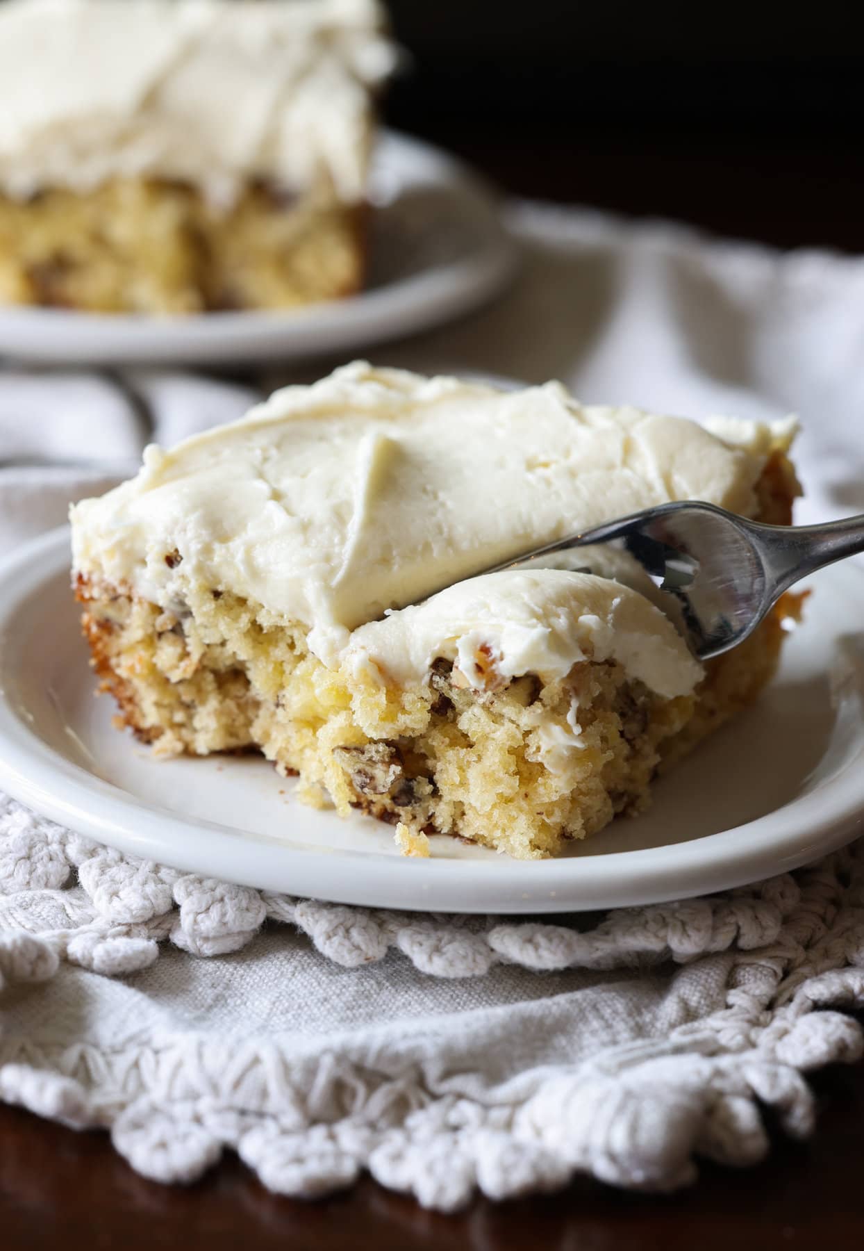 A square slice of pineapple sheet cake on a plate with a fork taking a bite