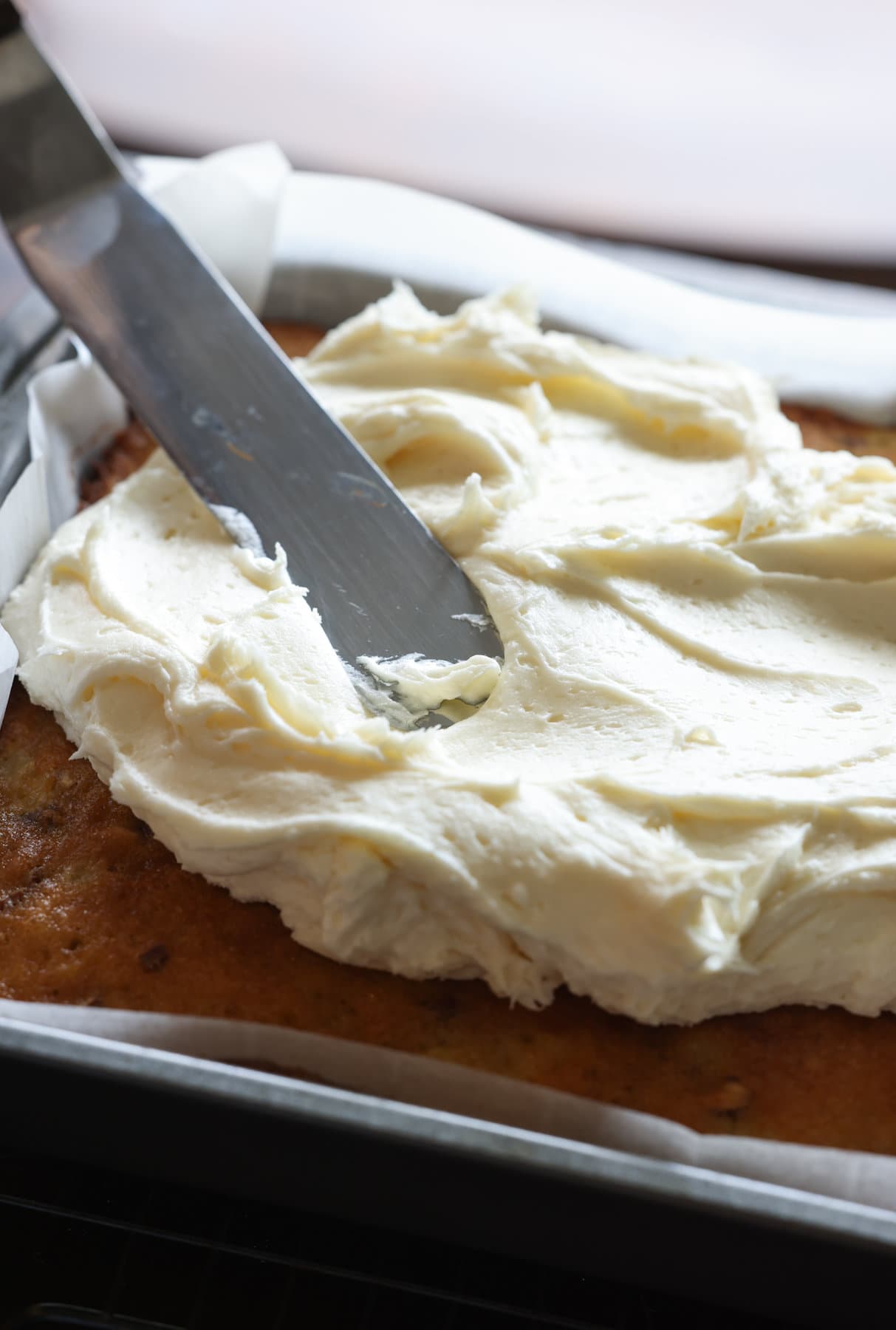 Spreading cream cheese icing onto a cake with an offset spatula