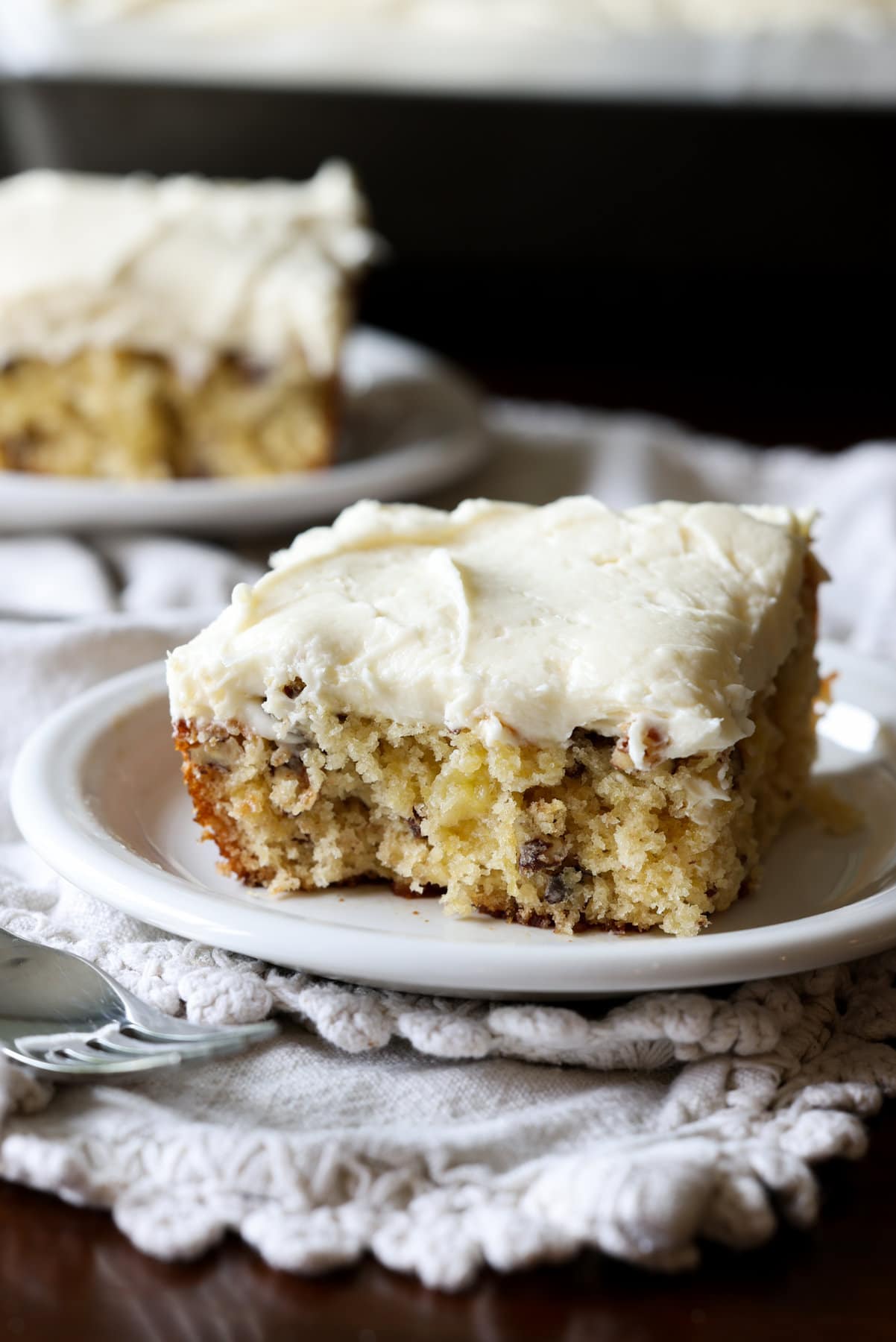 A slice of pineapple cake on a white plate topped with cream cheese frosting