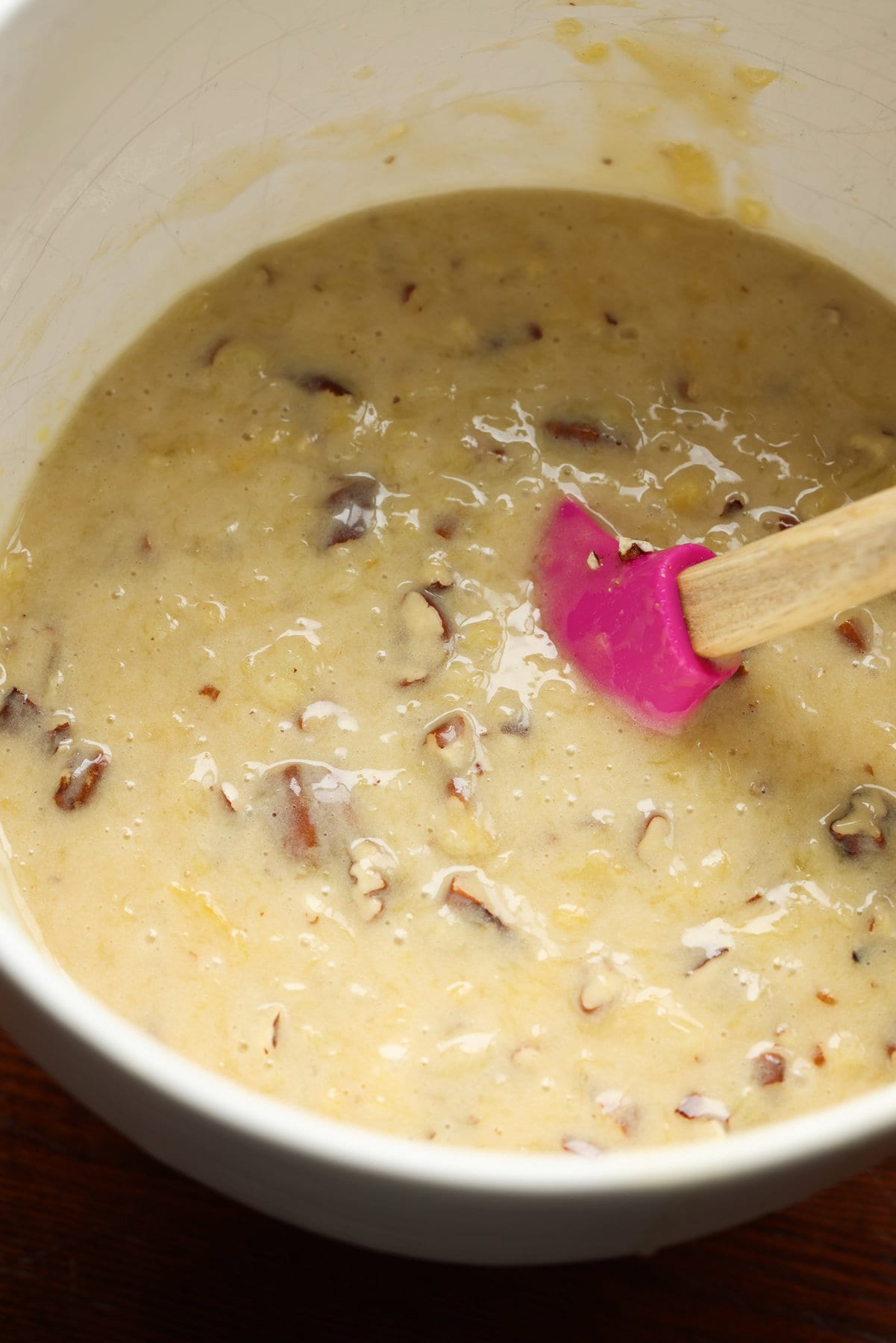 cake batter with nuts in a mixing bowl with a rubber spatula