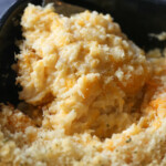 Close up of a corner of a casserole dish with a serving spoon removing a serving a cheese and potato casserole.