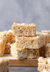 Rice Krispie Treats stacked on a wooden platter lined with parchment paper.