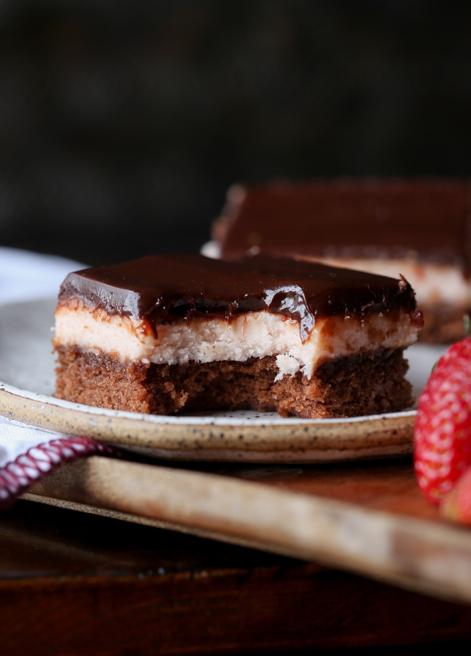 A fudge brownie topped with strawberry buttercream and chocolate ganache with a bite taken out on a plate