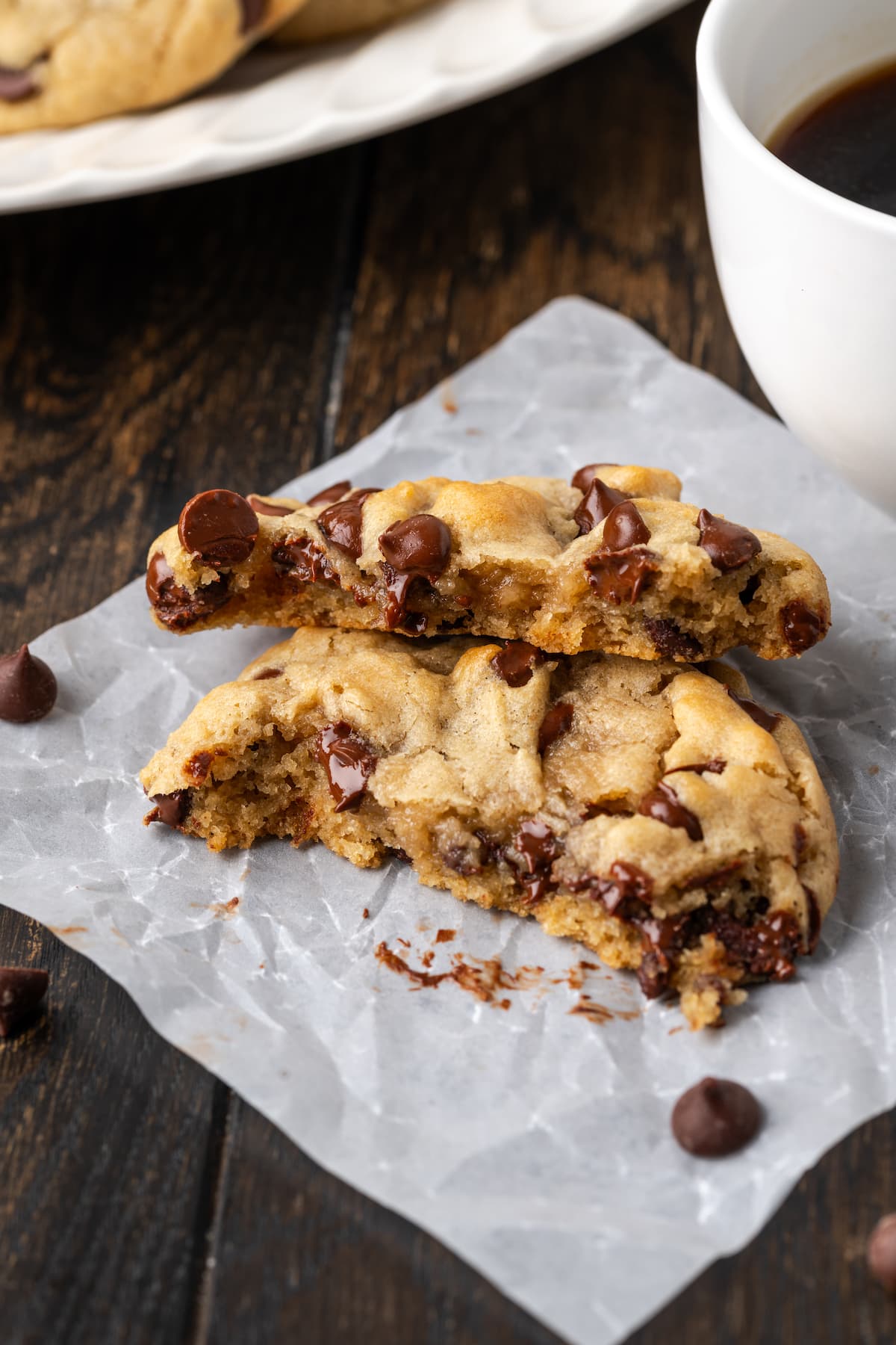 Two halves of a chocolate chip Subway cookie stacked on a piece of parchment paper next to a cup of coffee.