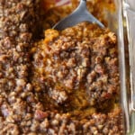 A serving spoon removing a scoop of sweet potato souffle from a baking dish.