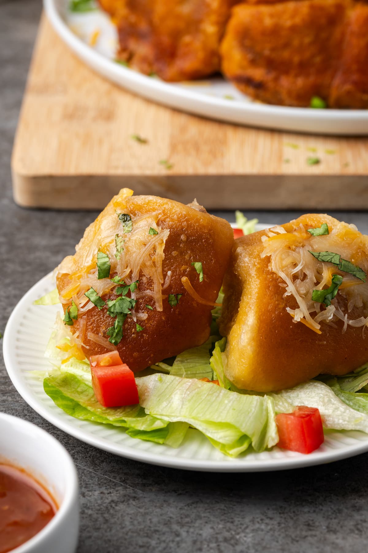 Two taco monkey bread bites on top of shredded lettuce and diced tomatoes on a white plate.