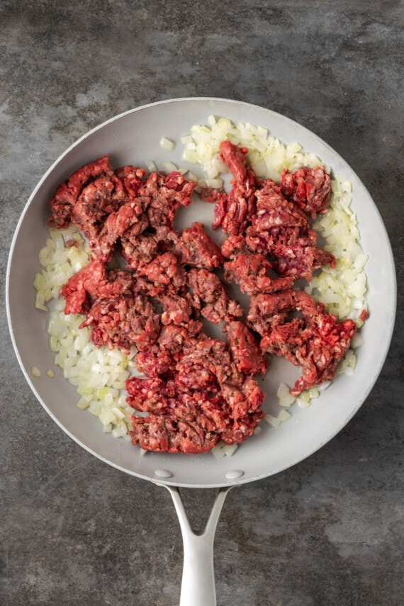 Ground meat added to diced onions in a skillet.