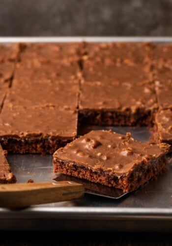 A slice of Texas sheet cake is lifted from a sheet pan with a spatula.