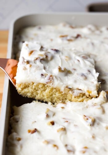 pulling a piece of white sheet cake from the pan with a spatula